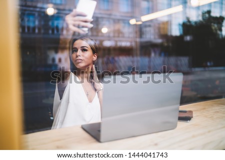 Beautiful woman using good internet connection for taking video in online application for blogging, attractive hipster girl holding smartphone gadget in hands and taking pictures for social network