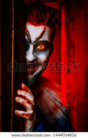 A close up portrait of an angry clown from a horror film hiding behind a door. Halloween, carnival.