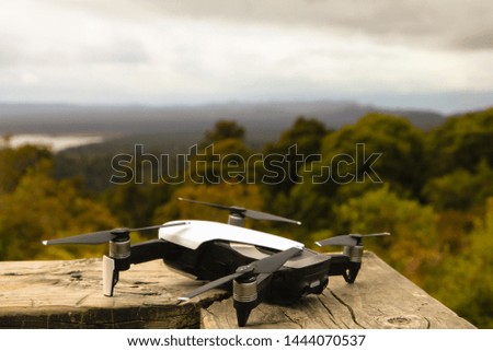 Little white drone lying on wooden handrail. Beautiful New Zealand nature. Cloudy, summer day.