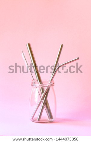 reusable stainless steel straws and cleaning brush in glass bottle on pink background, eco friendly lifestyle, copy space