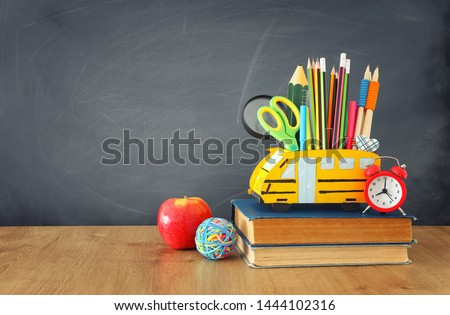 education and back to school concept. pencils stand as bus over wooden desk infront of classroom blackboard