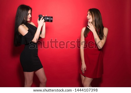 Two woman in night dresses take photo on photocamera standing on red background