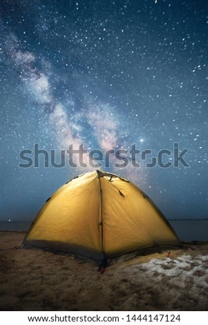 yellow tent standing at night against milky way and sea
