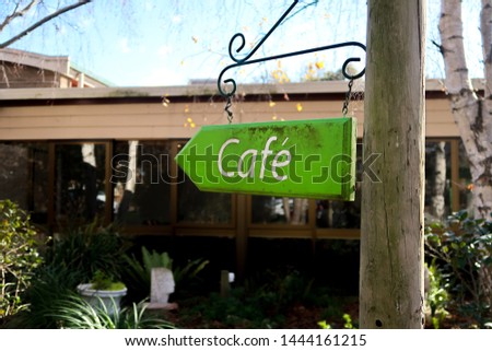Arrow shaped Cafe sign on post, soft focus background