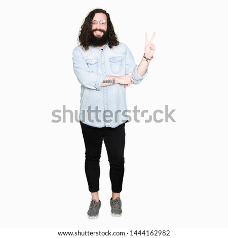Young hipster man with long hair and beard wearing glasses smiling with happy face winking at the camera doing victory sign. Number two.