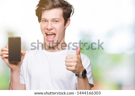 Young man showing smartphone screen over isolated background happy with big smile doing ok sign, thumb up with fingers, excellent sign