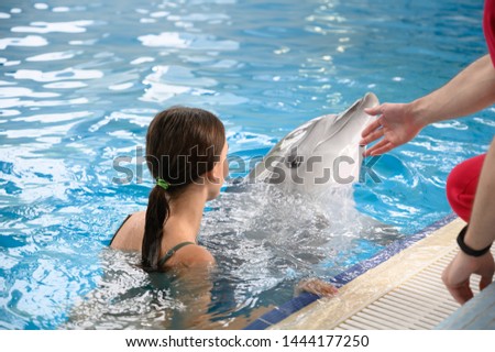 young beautiful brunette woman in a swimsuit swims and plays with a funny cute sea dolphin. Emotional rest in the water park. positive emotions, communication with marine mammals