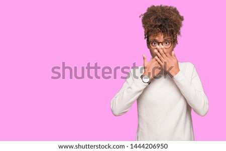 Beautiful young african american woman wearing glasses over isolated background shocked covering mouth with hands for mistake. Secret concept.