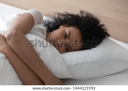 Sad depressed african american young woman hugging pillow lying in bed alone, upset frustrated black lady feeling lonely anxious suffer from insomnia trying to sleep thinking of problem in bedroom Royalty-Free Stock Photo #1444221992