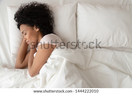 Serene calm african american woman sleeping in comfortable bed lying on soft pillow orthopedic mattress, peaceful young black lady resting covered with blanket on white sheets in bedroom, top view Royalty-Free Stock Photo #1444222010