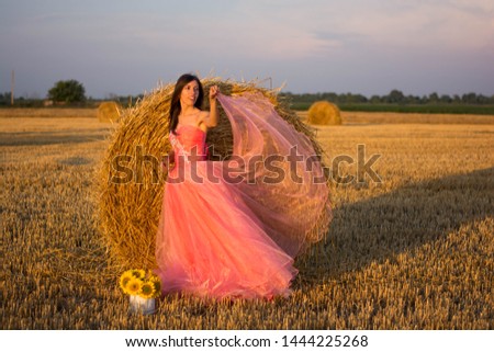 young woman in a beautiful pink dress dancing next to hay field nature