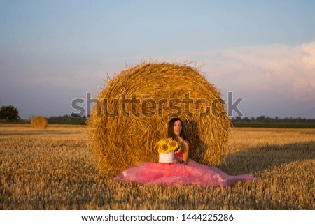 beautiful woman in a pink dress sitting on a hay with sunflowers in their hands a field of nature