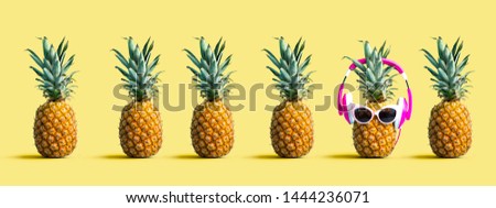 One out unique pineapple wearing headphones on a solid color background Royalty-Free Stock Photo #1444236071