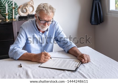 Senior old man elderly examining and signing last will and testament Royalty-Free Stock Photo #1444248611