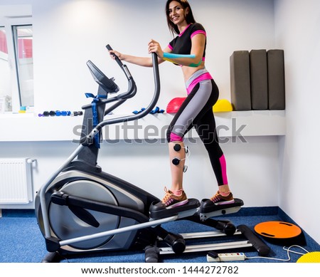 Young sports woman with electrostimulator on the muscles of the legs. Fitness training with an electrostimulator. Physiotherapy.