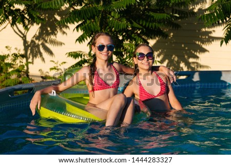 Happy young twins in sunglasses are having fun in swimming pool on an inflatable mattress and smiling, sunlight