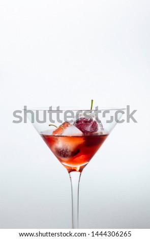 ice cubes with cherries inside into a red cocktail, white background with free space for text