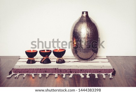 Cozy home interior decor, burning candles in coconut shell on a multi-colored rug with metal vase background
