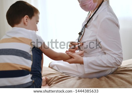 Vaccination of a child under five years old by a doctor at home. Demonstration of vaccination with a syringe in the hand of the boy.