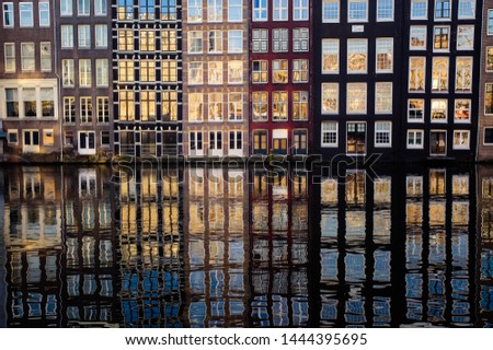 Facades of Damrak narrow houses and their reflection in the channel in Amsterdam