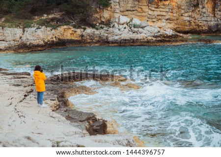 woman in yellow raincoat standing at rocky beach looking at see. copy space