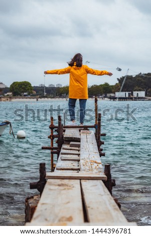 woman standing on the edge of the small fishing pier looking at storming sea. overcast weather