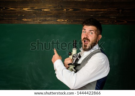 Happy teacher at auditorium. Young teacher with microscope near blackboard pointing at copy space. Male teacher in classroom. Teacher giving lesson to students. Education, high school, people concept.