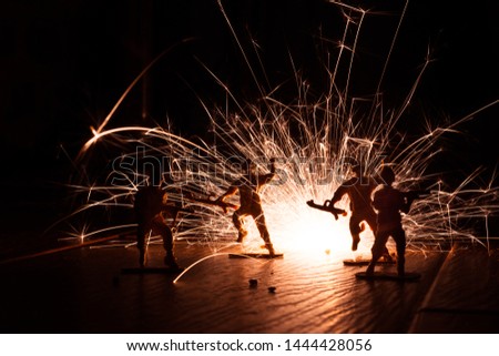 A photo of toy soldiers with a sparkler behind them simulating an explosion. Two of the soldiers appears as if they are jumping away from the explosion. This is a low light silhouette picture.