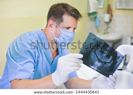 Male dentist in the medical office of the clinic holds an image of the RTG, x-ray with gloves, panoramic picture, wisdom teeth. Royalty-Free Stock Photo #1444430645