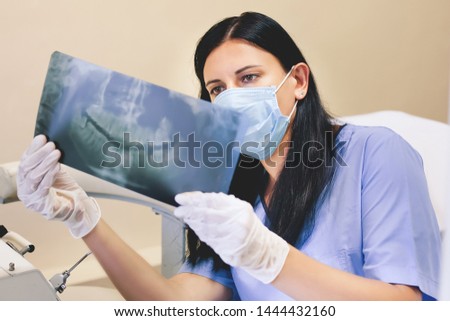 Beautiful young woman dentist in the medical office of the clinic holds an image of the RTG, x-ray panoramic picture, eighth teeth sideways in gloves and a mask Royalty-Free Stock Photo #1444432160
