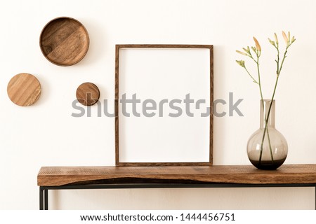 Stylish and modern scandinavian room interior with brown mock up poster frame, wooden console and rings on the wall, beautiful flowers in glassy vase. Design composition of home interior. Home decor.