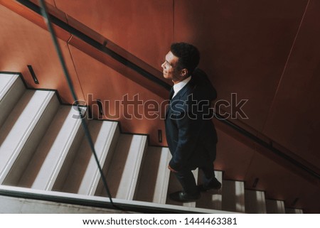 Focus on top view of jolly man in elegant classic suit. He is having fun while going upstairs to workplace. Copy space in left side