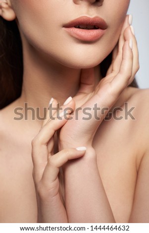Cropped portrait of attractive young lady with natural makeup keeping hands on her face