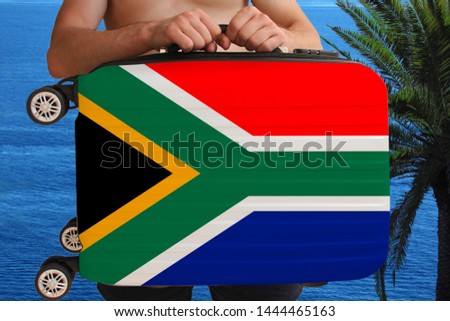 tourist holds with two hands a suitcase with the national flag of South Africa, a symbol of vacation, immigration, political asylum