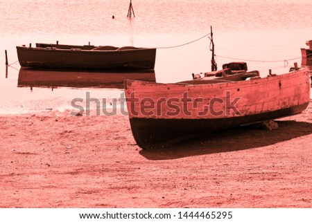 A wooden boat on shore and a boat in the water, monochromatic image, trendy color 2019 Coral.