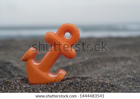Close up picture of a small orange anchor beach toy placed on the black sand at the Batu Bolong beach in Canggu, Bali during a cloudy day