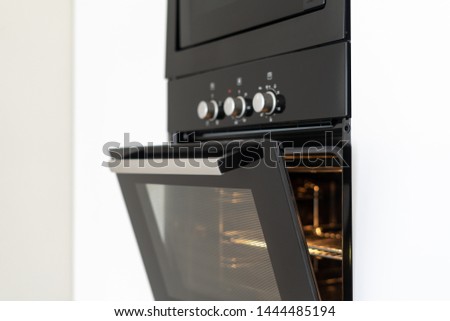 Selective focus of black and modern built in oven with open glass door on white contemporary kitchen