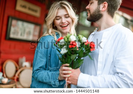 Cropped photo of happy bearded man gently hugging his positive young girlfriend while giving bouquet of flowers