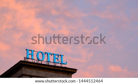 Weathered and burned out neon hotel sign lit up against a colorful and dramatic red and orange sky at sunset in New York