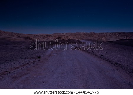 long exposure desert night scenery landscape with stars blue sky photography of wasteland country side gravel road go to mountains on horizon line background  