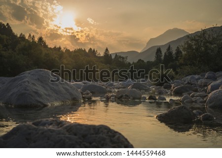 Beautiful summer evening with sun just setting down behnd julian alps and river in Resia region or Rezija, close to Resciutta village. Stones in the water in the close foreground