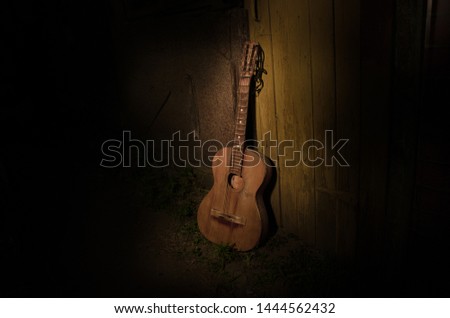 An wooden acoustic guitar is against a grunge textured wall. The room is dark with a spotlight for your copyspace. old broken guitar
