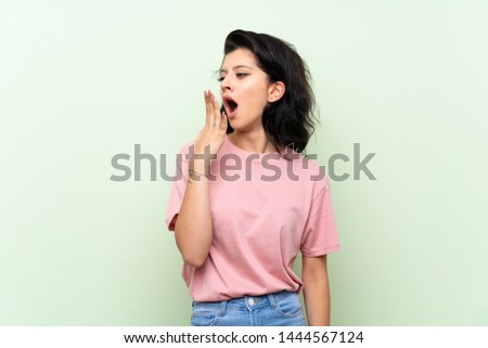 Young woman over isolated green background yawning and covering wide open mouth with hand