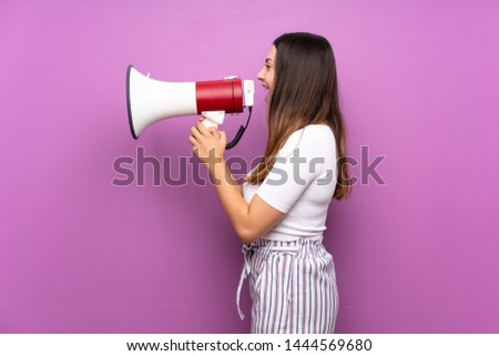 Young woman over isolated purple background shouting through a megaphone