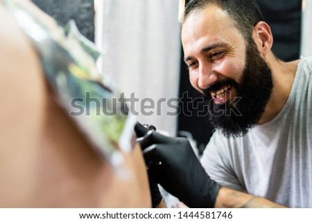 Professional master tattoo artist drawing tattoos picture on man's back using machine wearing black gloves at studio salon body art