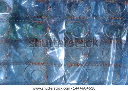 Spring mattress wrapped in plastic film wrap creates a geometric texture and a repetitive pattern with its circular spring wires. It is thrown out to the street as garbage.