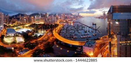 Aerial panorama of Hong Kong under moody sunset sky with crowded skyscrapers by Victoria Harbour & an elevated highway curving along the coastline between Causeway Bay Typhoon Shelter & an urban park