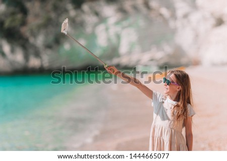 Little girl taking selfie by her smartphone on the beach. Kid enjoying her suumer vacation and making photos for memory