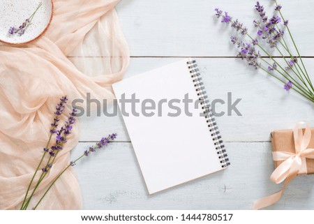 Blank paper notepad, pastel pink color blanket, lavender flowers and gift box on rustic blue wooden background. Top view, tender minimal flat lay style composition. Fashion blogger workspace desk.