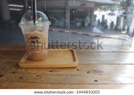 The close-up picture of a mocha coffee in a plastic glass on a wooden tray at a cafe on blur background